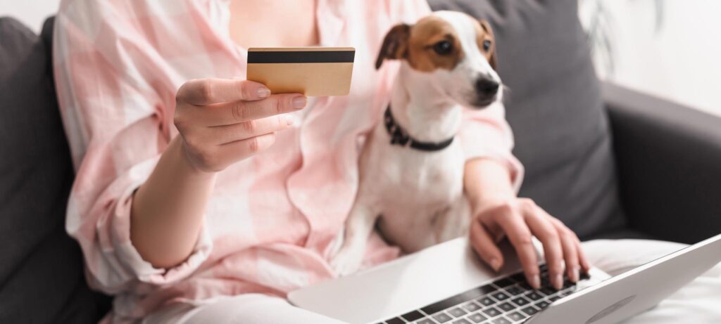 partial view of young woman holding credit card near dog and laptop while online shopping at home